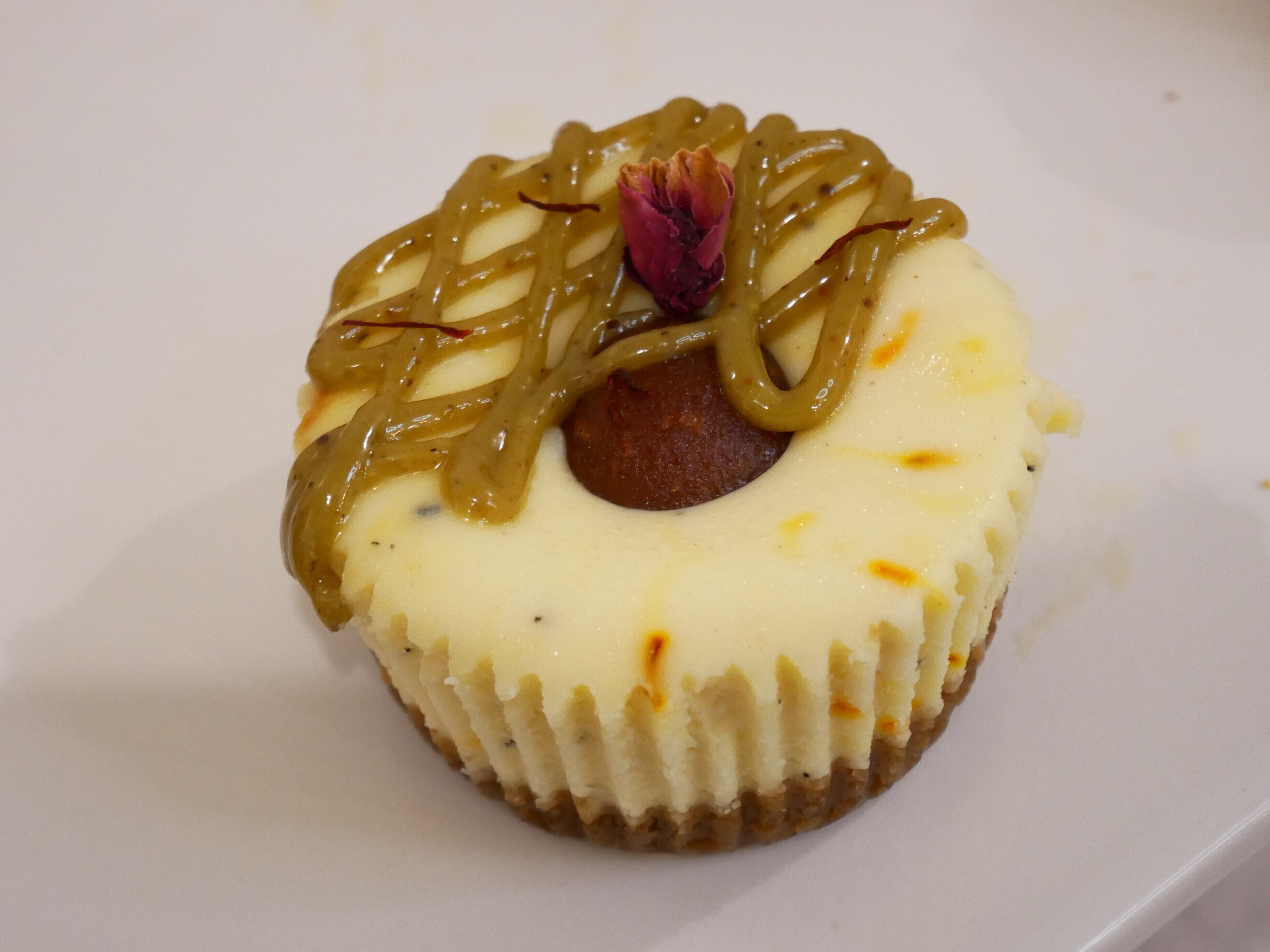Gulab jamun mini-cheesecake cupcake topped with caramel, and a decorative flower.